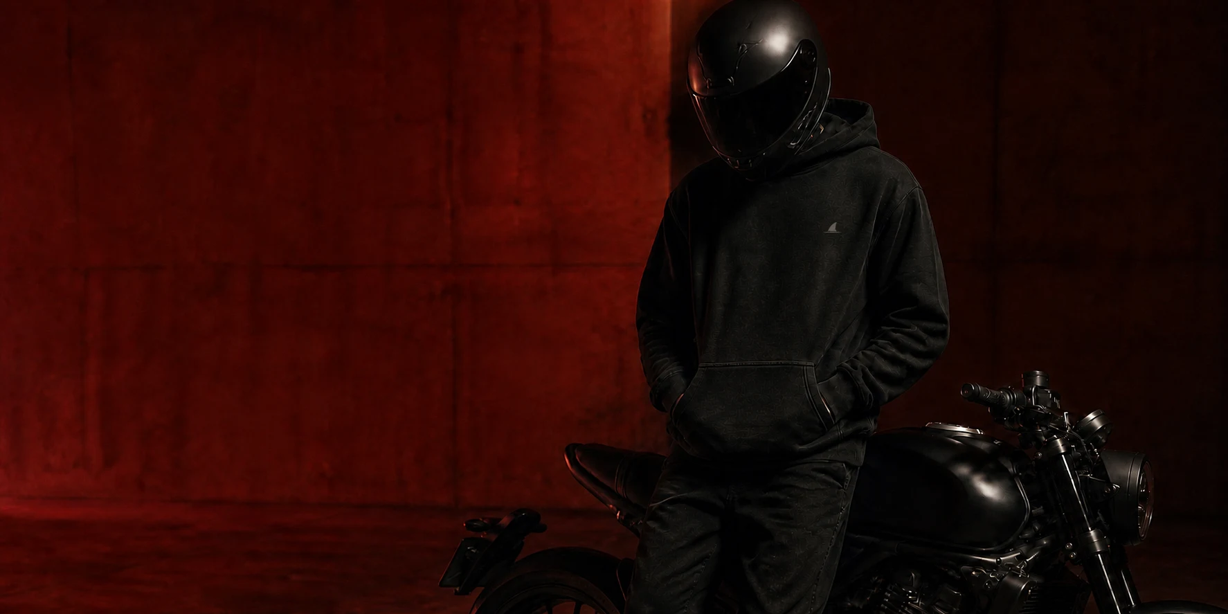 Helmeted rider wearing an Acheilus hoodie beside a motorcycle